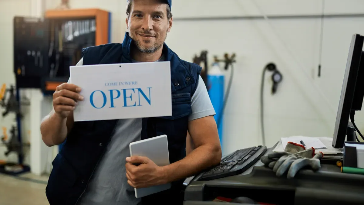 A local shop owner holding an Open sign at the door