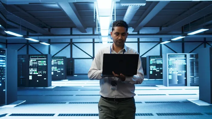 An engineer holding a laptop while walking through a data center