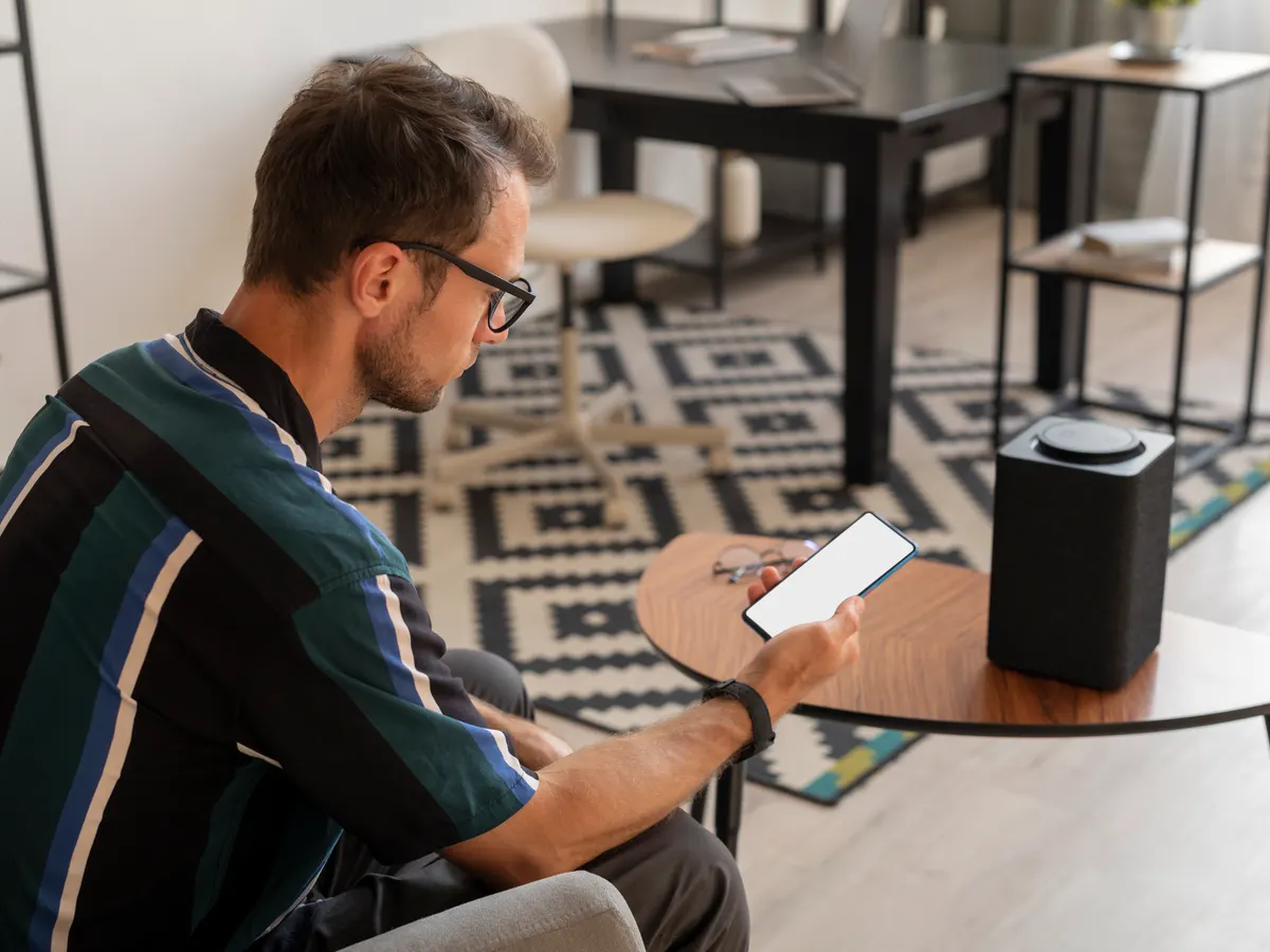 A man using his phone next to a smart speaker at home