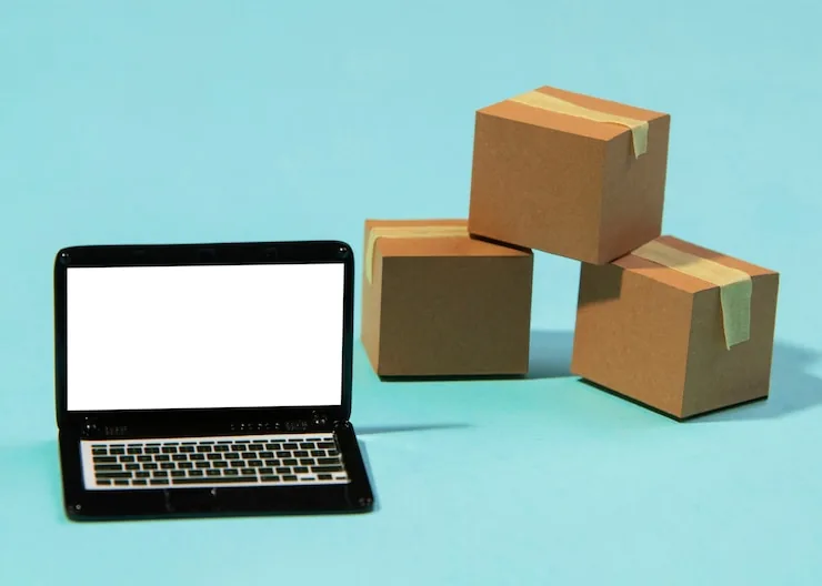 A laptop next to stacked cardboard shipping boxes