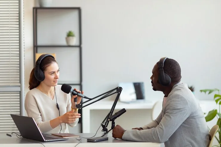 A man and a woman recording a podcast interview with microphones
