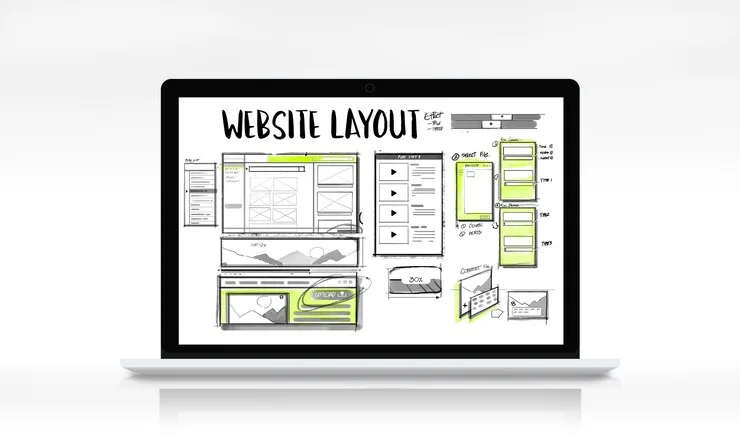 A laptop showing a website layout sketch with page sections and wireframes