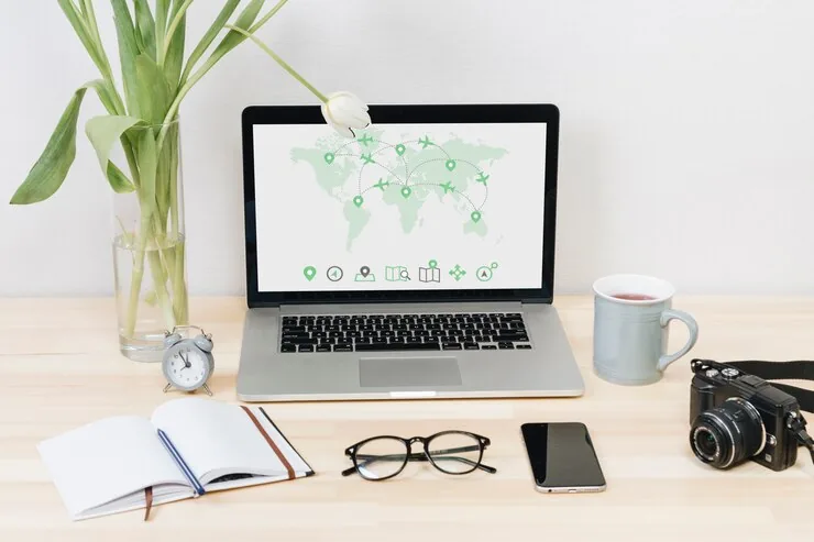 A laptop showing a world map on a desk with a notebook and camera